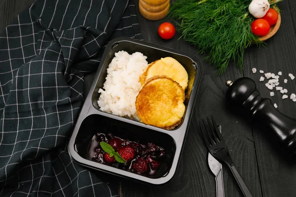 Rice porridge with cakes and berry jam in black plastic box