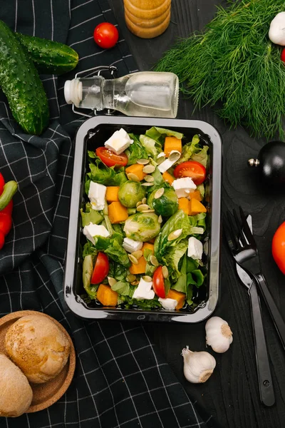 Fresh vegetable salad in plastic container on black wooden table