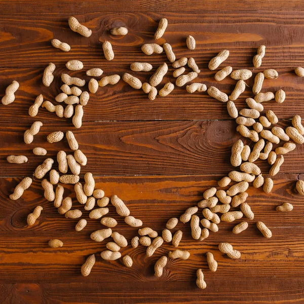Pile of whole peanuts in heart shape on wooden background