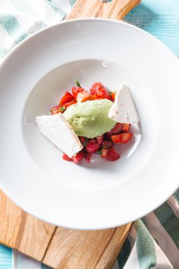 Doğranmış çilek ile fıstıklı dondurma ve meringues beyaz tabakta servis