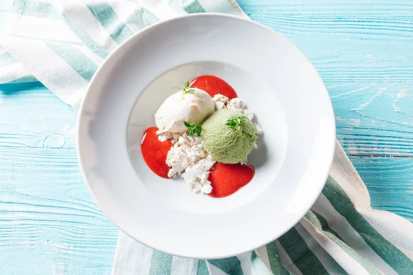 Top view of pistachio and cream ice-cream served with crushed meringues and strawberry sauce