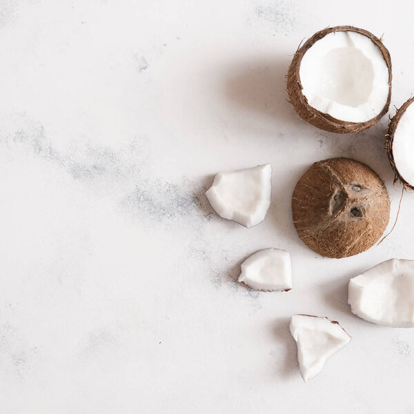 Top view of broken coconut pieces on white stone background