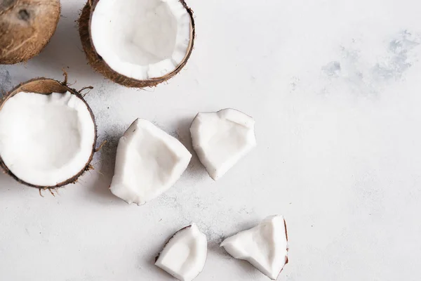 Top view of broken coconut pieces on white stone background