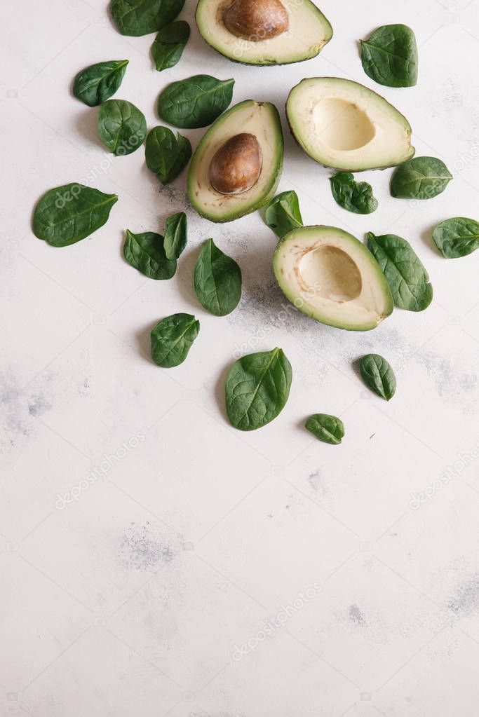 Top view of cutted avocados with basil green leaves on white concrete background