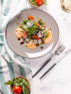 Plaka üzerinde soslu taze salata ahtapot, domates, roka ve soğan ile servis