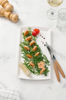 Izgara karides roka, limon dilimi ve beyaz tabakta domates ile servis