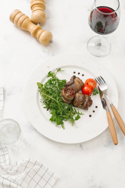 Meat rolls served with fresh arugula and tomato on white plate