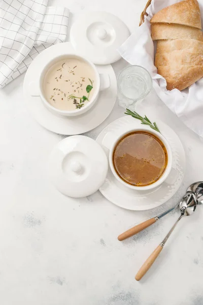 Two kinds of cream soup served with herbs on white background