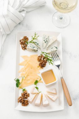 Beyaz masa üzerinde beyaz şarapla peynir tabağı fındık ve bal ile servis