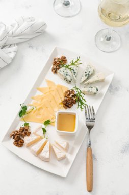 Beyaz masa üzerinde beyaz şarapla peynir tabağı fındık ve bal ile servis