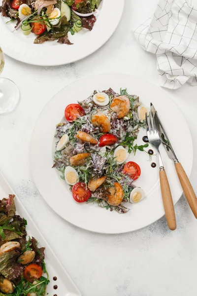 Yeşil salata domates, bıldırcın yumurtası ve beyaz plaka üzerinde Kızarmış karides ile