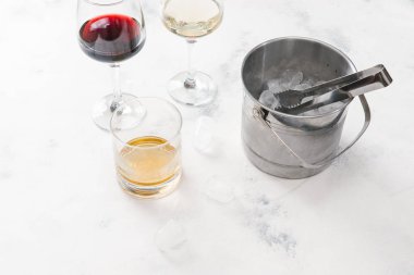 Kırmızı ve beyaz şarap, viski ve pot beyaz beton zemin üzerine buz küpleri ile cam gözlükler