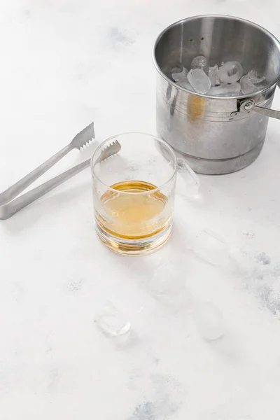 Glass of whiskey with ice cubes on white concrete background