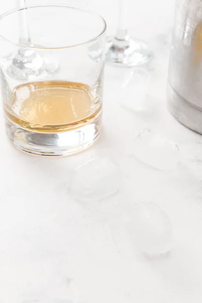 Glass of whiskey with ice cubes on white concrete background