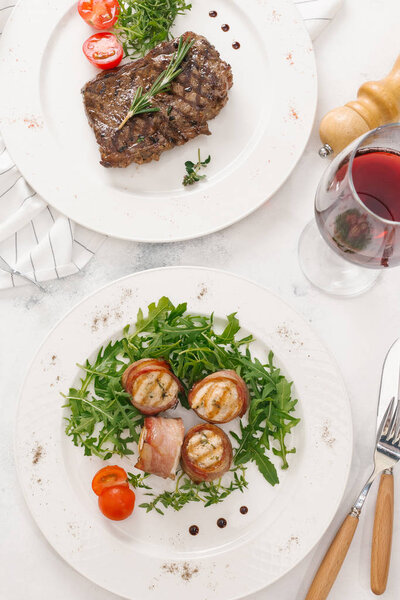 Top view of beefsteak and bacon rolls served with arugula and rosemary twig on white plates