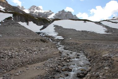 Kayalık dağ yamaçlarında kar küçük su akışı ile kaplı doğal görünümünü