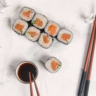 Somon ve salatalık ile geleneksel Japon rulo chopsticks ve ışık gri taş zemin üzerine soya sosu ile servis