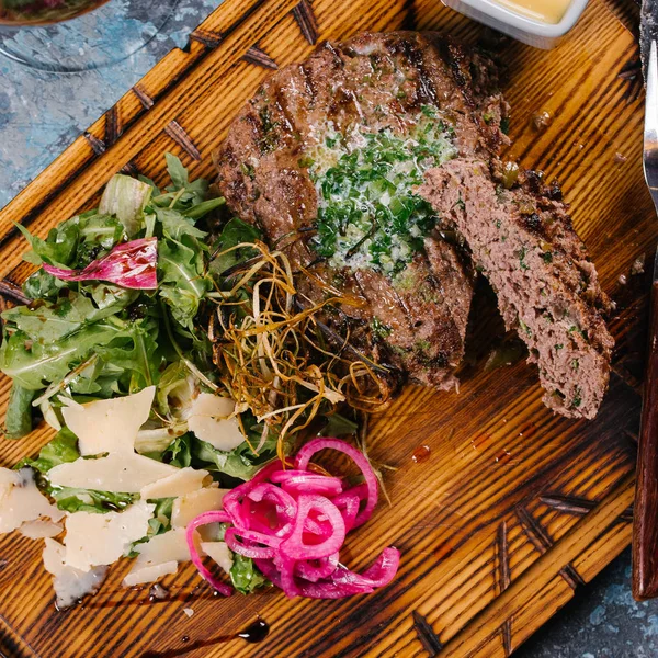 Grilled patty cake served with arugula salad and cheese on wooden board