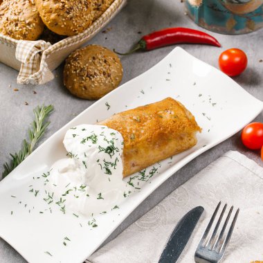 Ekşi krema ve beyaz tabakta dereotu ile doldurulmuş krep servis