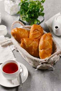 Hasır sepet gri taş zemin üzerine çay ile servis içinde taze pişmiş çörekler