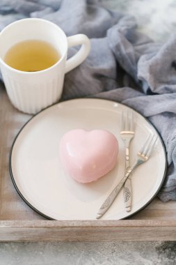 Pembe sufle pastane beyaz plaka üzerinde kalp şeklinde ahşap tepsi üzerinde yeşil çay ile servis