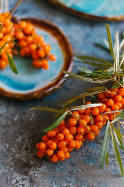 Mavi beton zemin üzerine el yapımı seramik plaka üzerinde taze olgun turuncu sandthorn görünümü Kapat