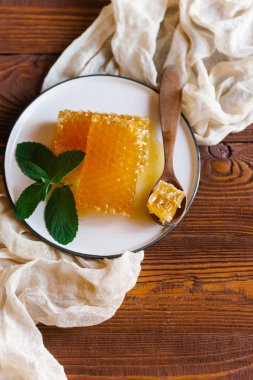 Bej keten kumaş nane dal beyaz plaka üzerinde tahta kaşıkla üstten görünüm taze peteğin süslenmiş