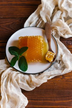 Taze peteğin süslenmiş beyaz plaka üzerinde tahta kaşıkla nane yaprakları üzerinde bej keten kumaş üstten görünüm