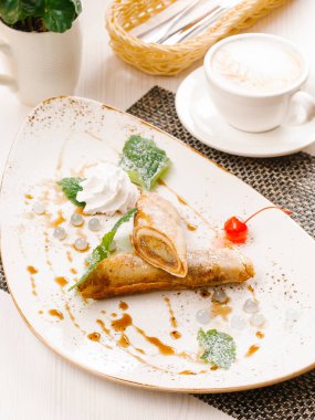 Haddelenmiş krep nane yaprakları ile hizmet, çırpılmış krema ve karamel şurup beyaz plaka üzerinde