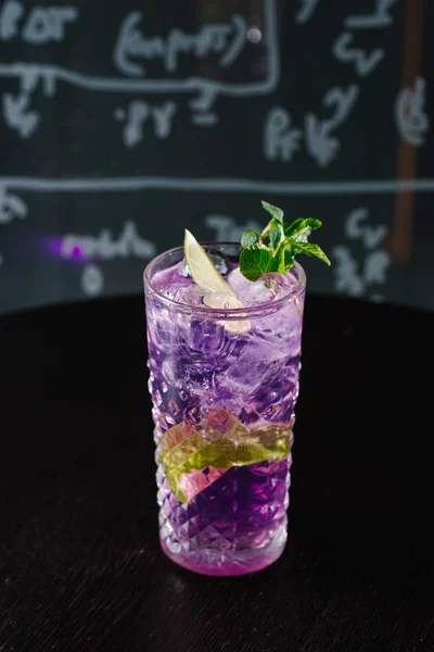 close up view of purple cocktail with mint on dark backdrop