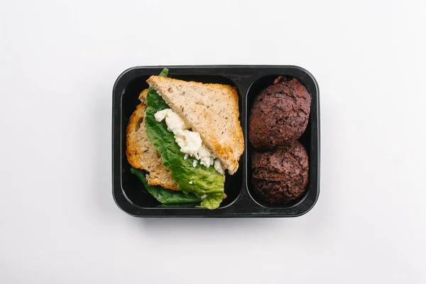 Top view of proper nutrition of sandwiches and cupcakes in box on white background