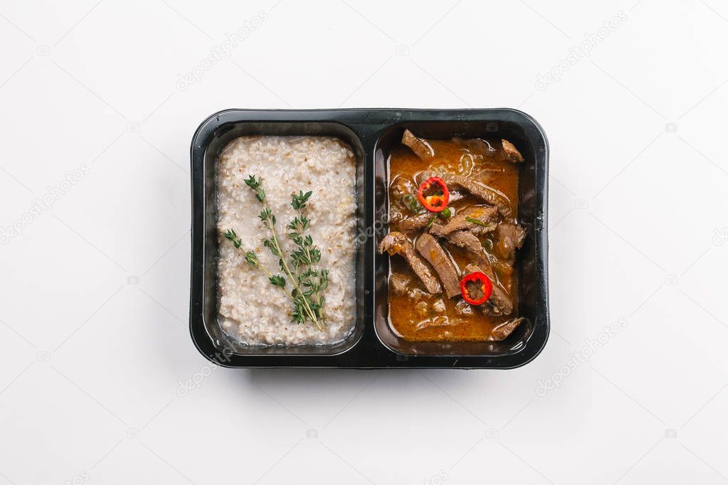 Top view of proper nutrition with porridge and meat in sauce in box on white background