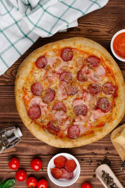 ahşap masa üzerinde pişmiş Pizza domates sosu, peynir, dilimlenmiş sosis ve pastırma ile üstten görünüm