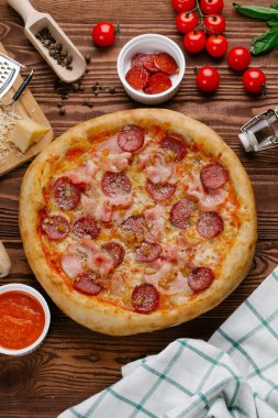 ahşap masa üzerinde pişmiş Pizza domates sosu, peynir, dilimlenmiş sosis ve pastırma ile üstten görünüm