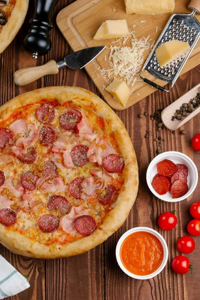 ahşap masa üzerinde pişmiş Pizza domates sosu, peynir, dilimlenmiş sosis ve pastırma ile üstten görünüm