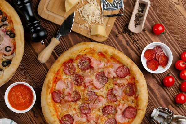 ahşap masa üzerinde pişmiş Pizza domates sosu, peynir, dilimlenmiş sosis ve pastırma ile üstten görünüm
