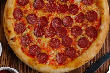 domates sosu, peynir ve dilimlenmiş sosis pişmiş pizza üstten görünüm ahşap tablo