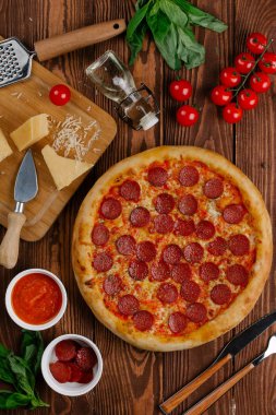 domates sosu, peynir ve dilimlenmiş sosis pişmiş pizza üstten görünüm ahşap tablo