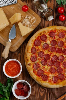 domates sosu, peynir ve dilimlenmiş sosis pişmiş pizza üstten görünüm ahşap tablo