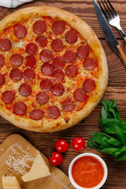 domates sosu, peynir ve dilimlenmiş sosis pişmiş pizza üstten görünüm ahşap tablo