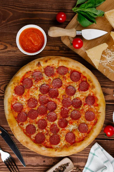 domates sosu, peynir ve dilimlenmiş sosis pişmiş pizza üstten görünüm ahşap tablo