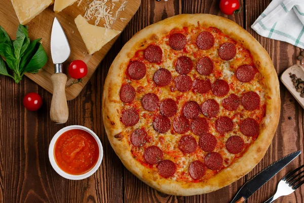 domates sosu, peynir ve dilimlenmiş sosis pişmiş pizza üstten görünüm ahşap tablo