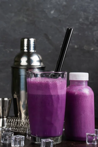 玻璃杯和一瓶紫色饮料和鸡尾酒摇床与冰块在桌子上 静生活 — 图库照片