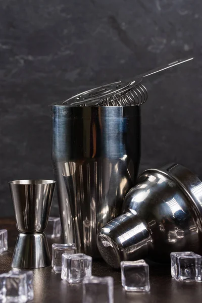 Stainless cocktail shaker and bar utensils with ice cubes on table, still life