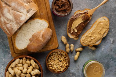 ahşap kesme tahtası üzerinde ekmek üst görünümü, koyu gri masa üzerinde çikolata krema ve fıstık ezmesi