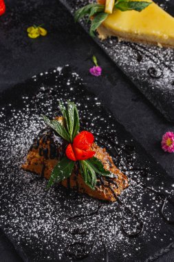 Koyu arka plan üzerinde arduvaz üzerinde servis lezzetli süslenmiş kek parçaları