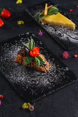 Koyu arka plan üzerinde arduvaz üzerinde servis lezzetli süslenmiş kek parçaları