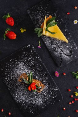 Koyu arka plan üzerinde arduvaz üzerinde servis lezzetli süslenmiş kek parçaları