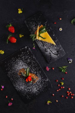 Koyu arka plan üzerinde arduvaz üzerinde servis lezzetli süslenmiş kek parçaları