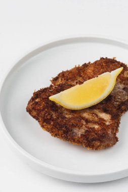 Beyaz bir arka plan üzerinde bir tabakta limon ile ekmekli ve kızarmış tavuk eti